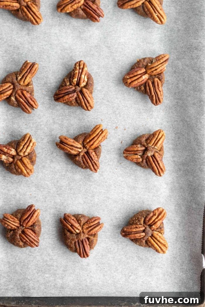 Date balls topped with three pecan halves each, arranged on a baking tray lined with parchment paper, ready for chocolate.