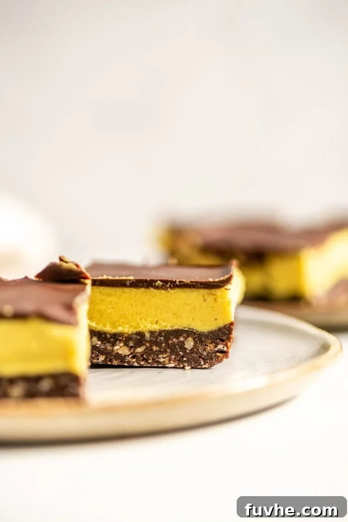 Vegan Nanaimo Bar Delight 3 Close up of squares of vegan Nanaimo bar on a small plate. More bars can be seen in the background.