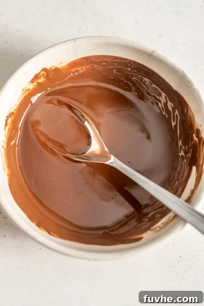 Vegan Nanaimo Bar Delight 9 Melted chocolate in a bowl with a spoon.