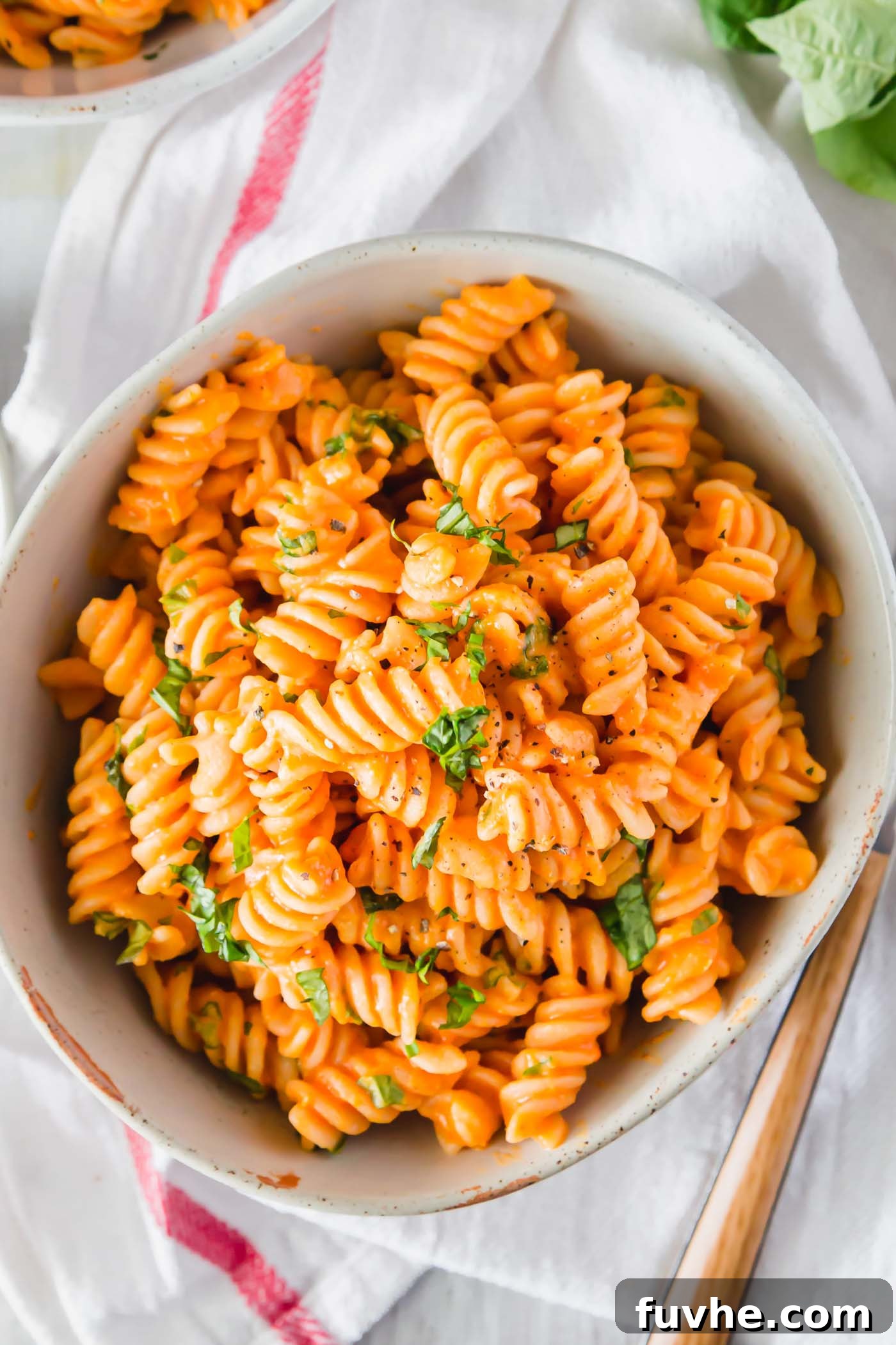 Overhead view of a bowl of creamy vegan roasted red pepper pasta topped with chopped fresh herbs, ready to be enjoyed.