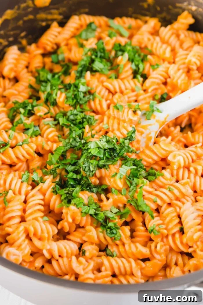 Roasted red pepper pasta garnished with fresh parsley, tossed in a large skillet, glistening with creamy sauce.