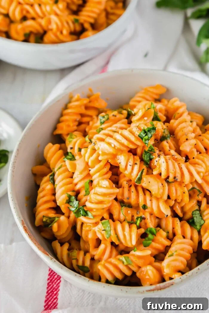 A close-up shot of a perfect bowl of vegan roasted red pepper pasta, artfully garnished with fresh herbs, ready to be savored.