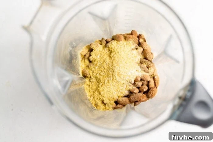 Plant-Based Parm Perfection 4 Nutritional yeast and raw almonds being combined in a blender, illustrating the simple preparation process.