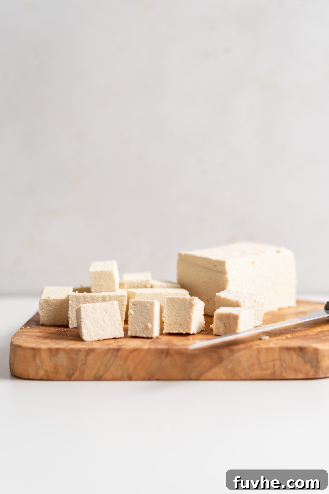 Freshly cut cubes of firm tofu on a wooden cutting board, ready for pressing or cooking.