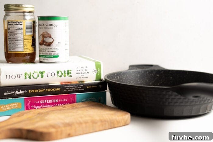 A DIY tofu press setup with a cutting board, black frying pan, and a stack of books with two cans on top.