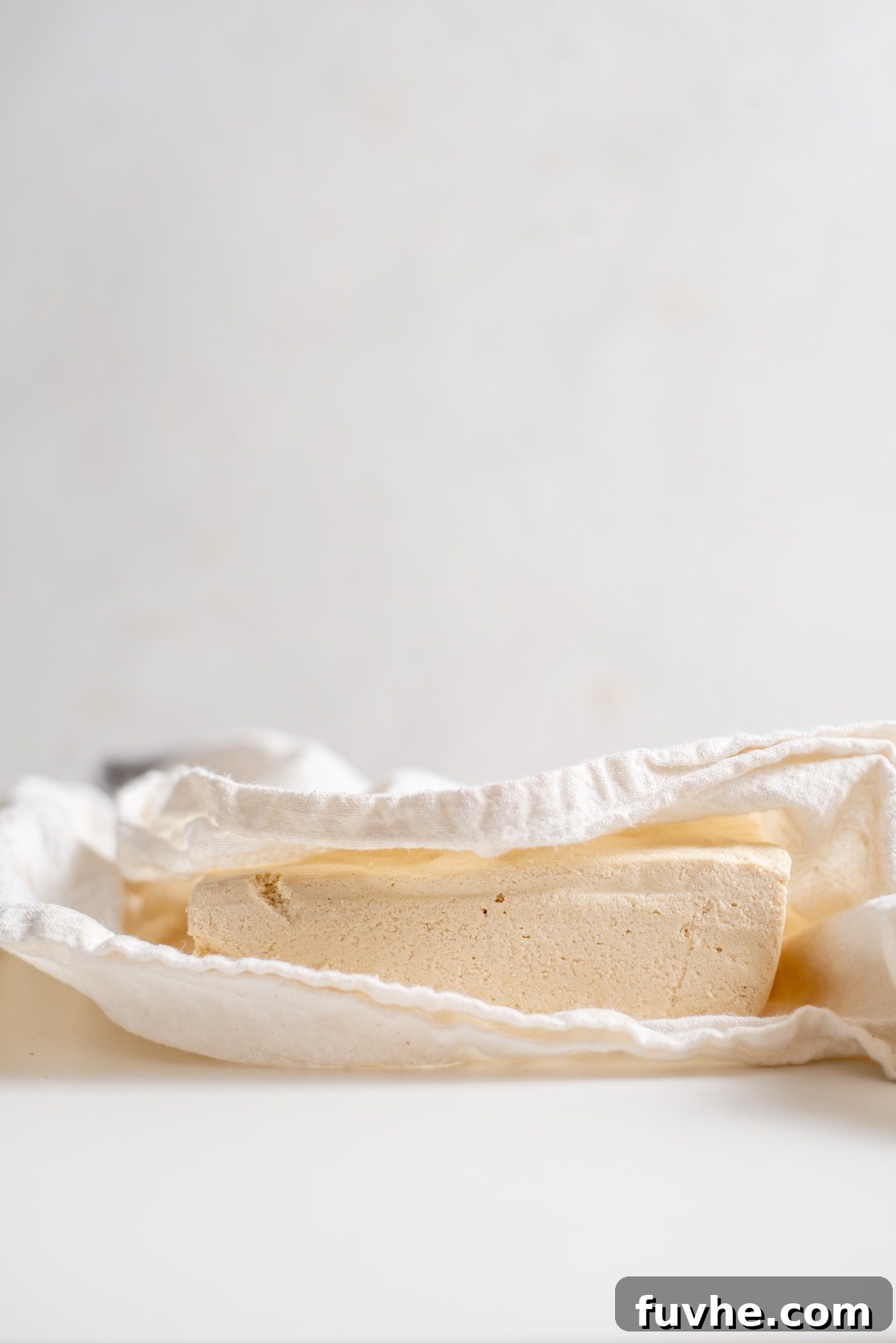 A block of tofu wrapped in a white dish cloth, ready for pressing.
