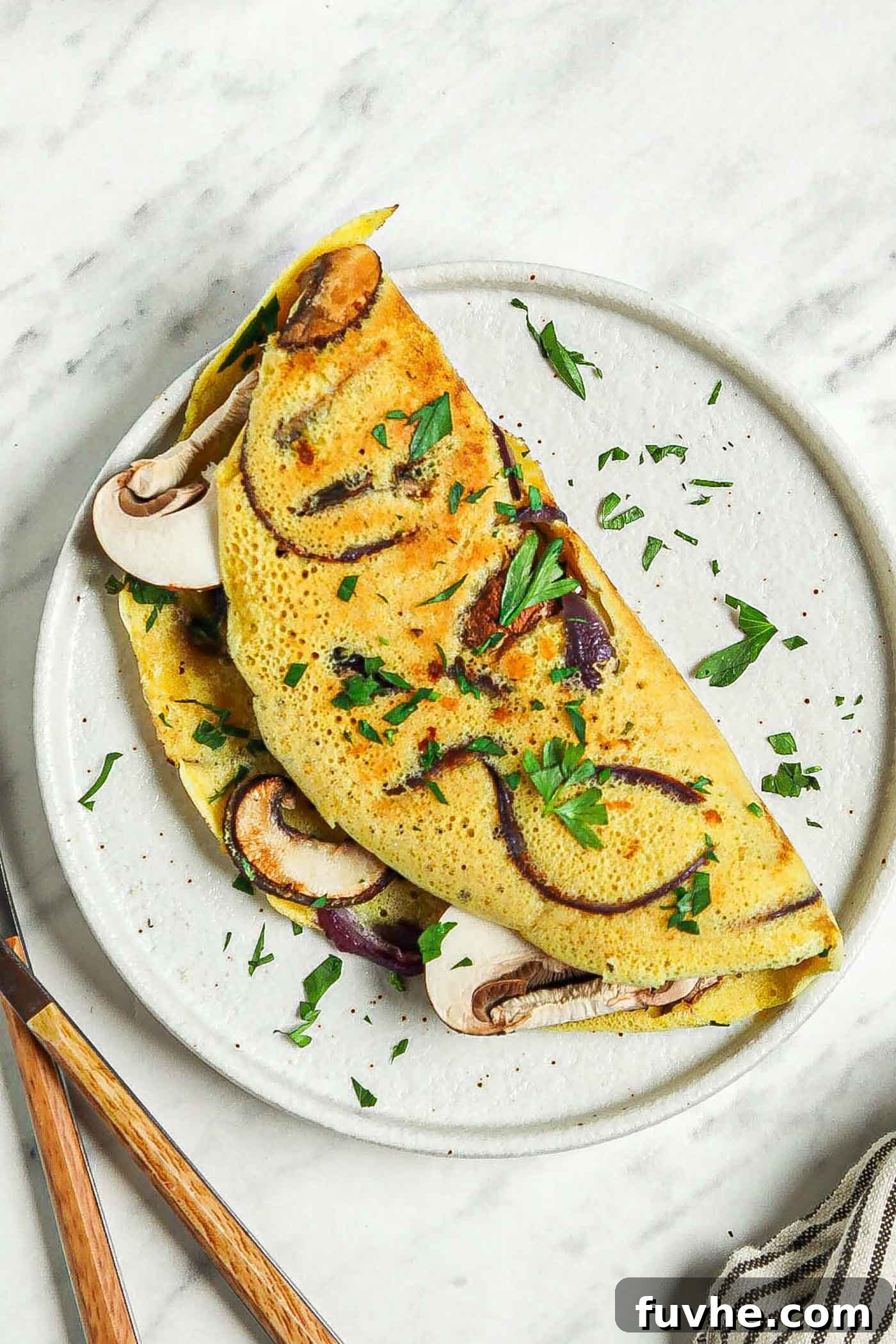 Fluffy Plant-Based Chickpea Omelette 2 Overhead view of a chickpea flour omelette filled with mushroom and onion on a plate.