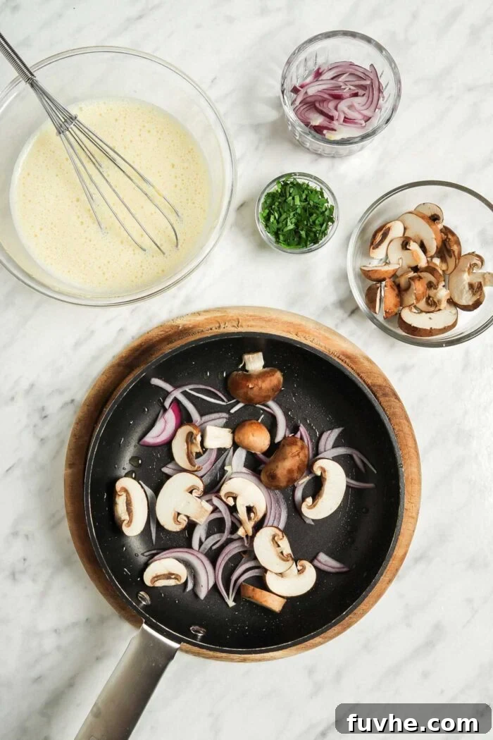 Fluffy Plant-Based Chickpea Omelette 5 Mushrooms and onions cooking in a hot pan. A glass mixing bowl of batter sits beside the pan.