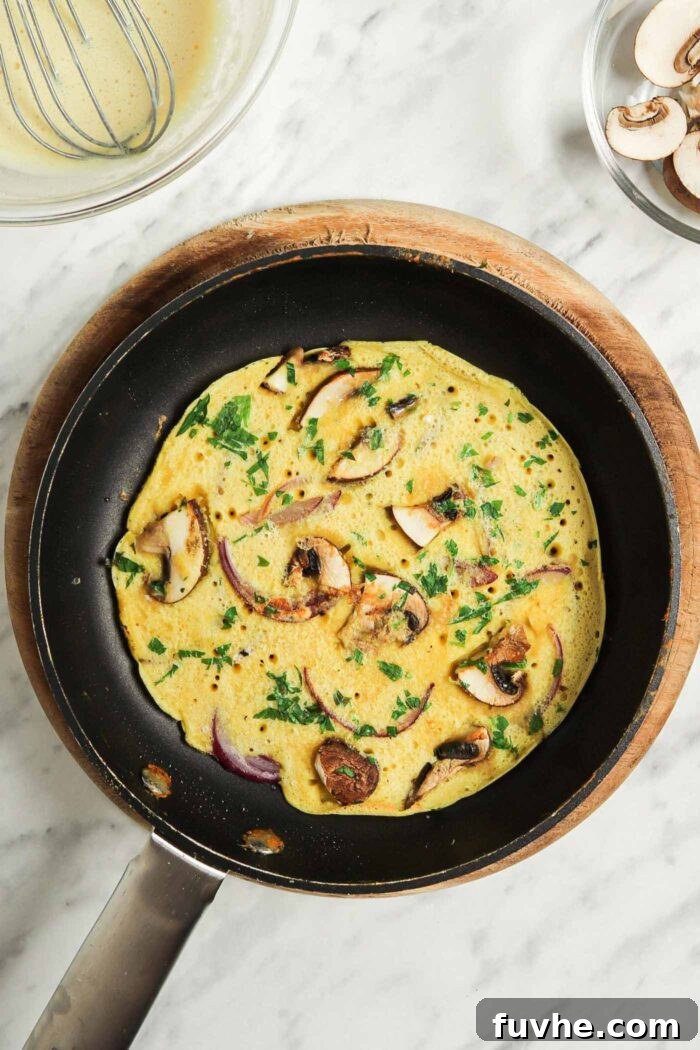 Fluffy Plant-Based Chickpea Omelette 7 Cooked chickpea omelette with parsley, red onion and mushroom in a small non-stick pan.