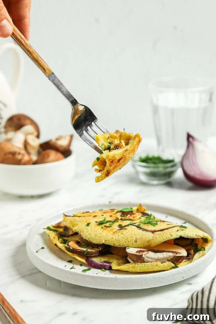 Fluffy Plant-Based Chickpea Omelette 8 Fork taking a bite of a chickpea flour omelette that's filled with mushroom, parsley and onion.
