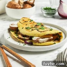 Fluffy Plant-Based Chickpea Omelette 9 Chickpea flour omelette stuffed with mushroom and onions on a plate.