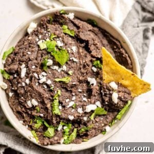 Large bowl of refried black beans topped with cilantro and feta cheese with a tortilla chip in it.