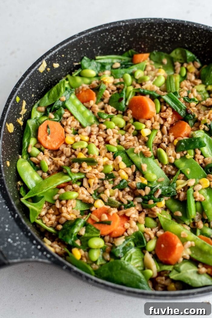Fried farro and assorted vegetables sizzling in a large skillet, highlighting the textures and vibrant colors.