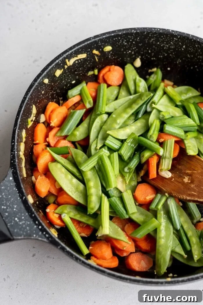 Carrots, green onions, and snow peas cooking in a skillet with ginger, showcasing the vibrant colors.