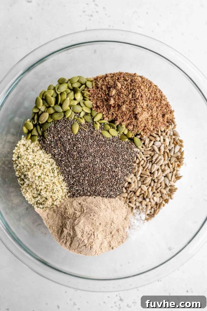 A close-up shot of a variety of raw, natural seeds beautifully mixed together in a large, light-colored mixing bowl, showcasing the primary dry ingredients for the seed bread recipe.