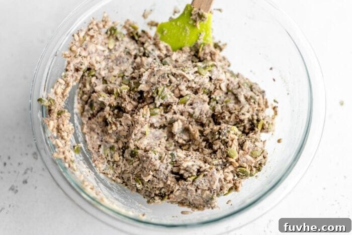 The raw seed bread dough, thick and rustic, resting in a mixing bowl with a spatula, indicating it's perfectly mixed and ready for the next step of baking.