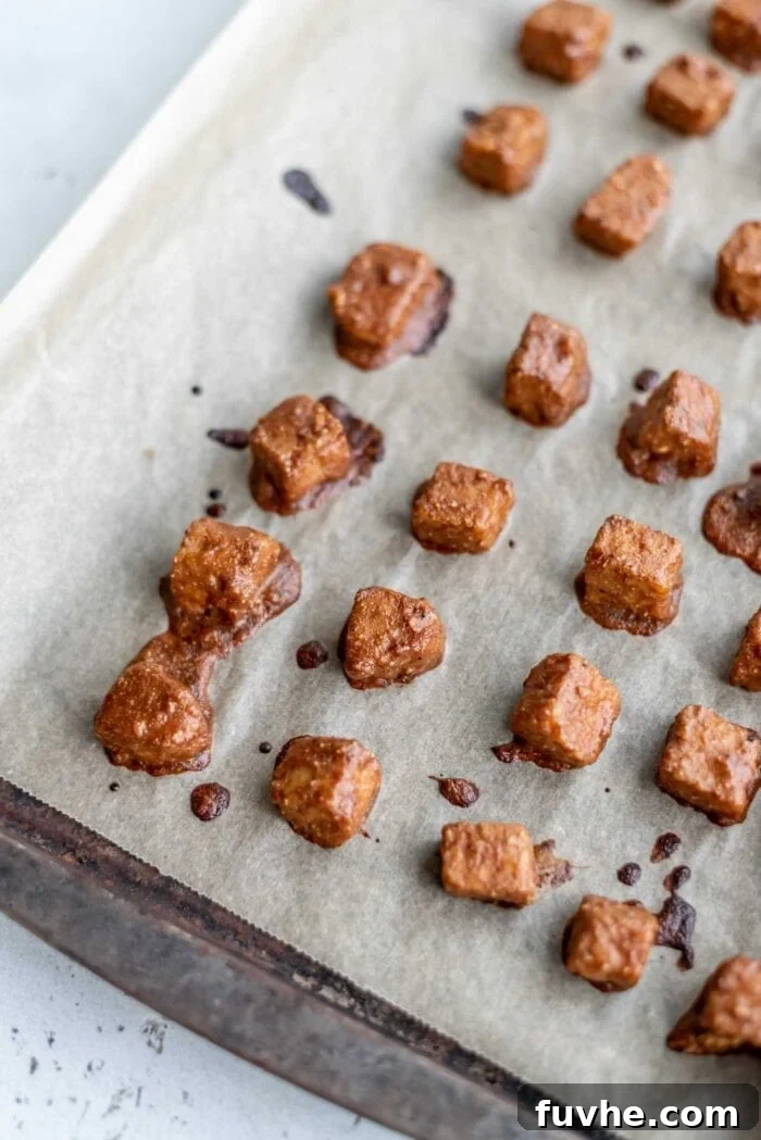 Wholesome Vegan Tempeh Buddha Bowl 4 Marinated, baked tempeh pieces spread evenly on a baking tray lined with parchment paper, showcasing their sticky and crispy texture.