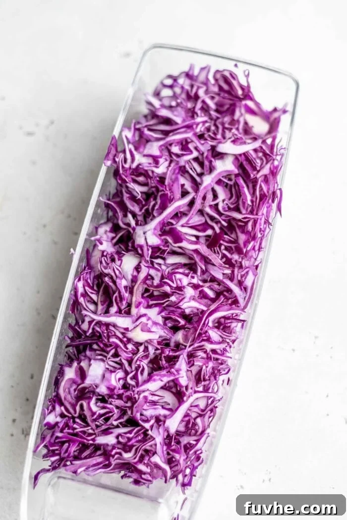 Wholesome Vegan Tempeh Buddha Bowl 5 Finely sliced red cabbage neatly contained in a mandolin slicer's collection tray, illustrating precise preparation.
