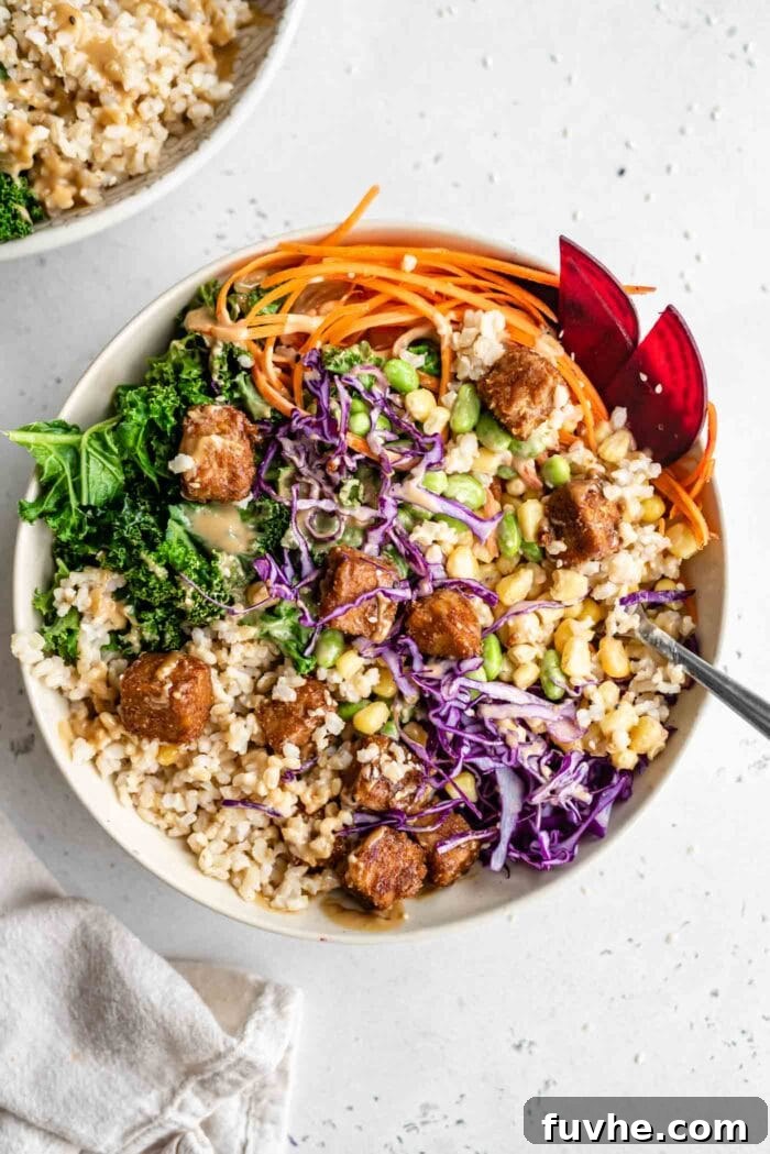 Wholesome Vegan Tempeh Buddha Bowl 7 A fully assembled vegan tempeh buddha bowl featuring an inviting arrangement of brown rice, edamame, tempeh, carrot, corn, kale, and red cabbage, elegantly topped with dressing and sesame seeds.