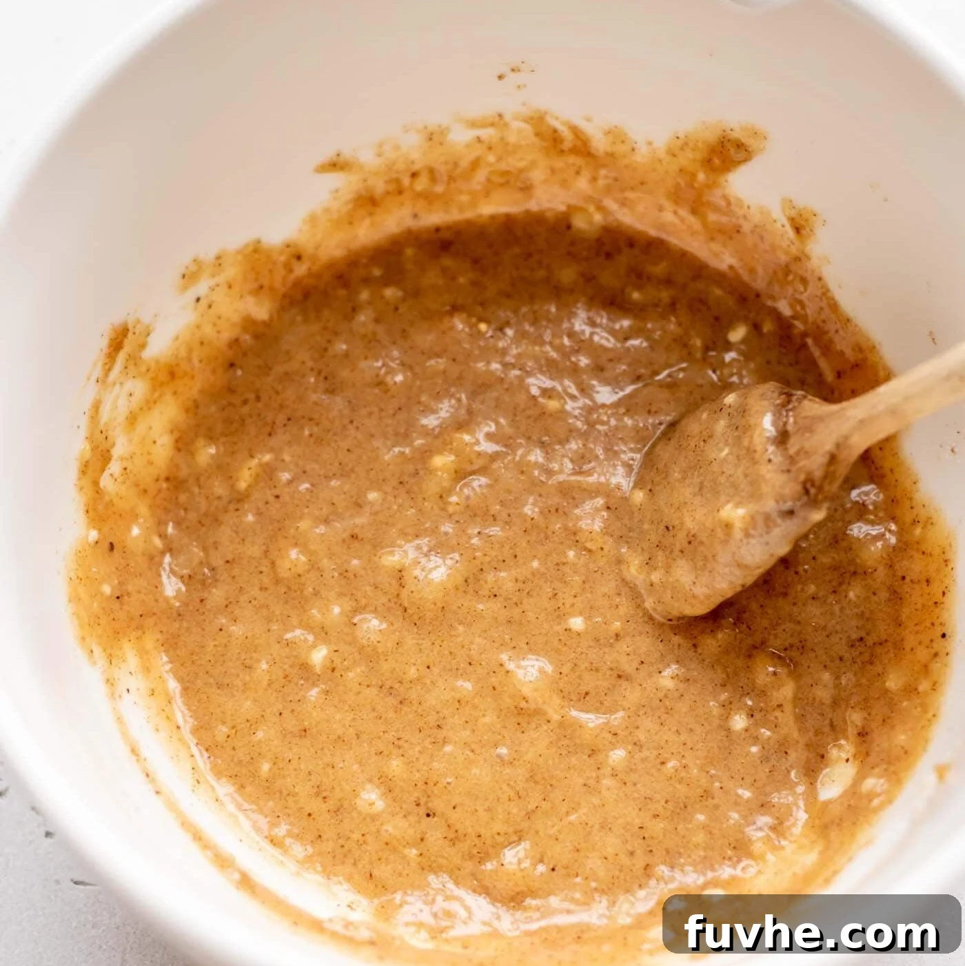 Mashed banana mixed with almond butter in a mixing bowl with a spoon, demonstrating the well-combined wet ingredients.