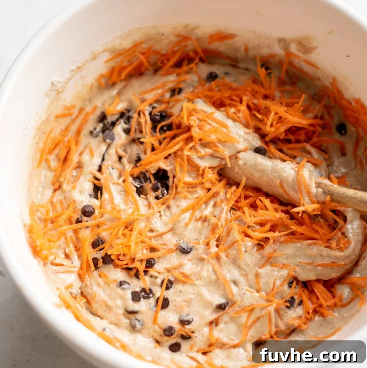 Raw muffin batter with chocolate chips and grated carrot in a mixing bowl, ready for baking.