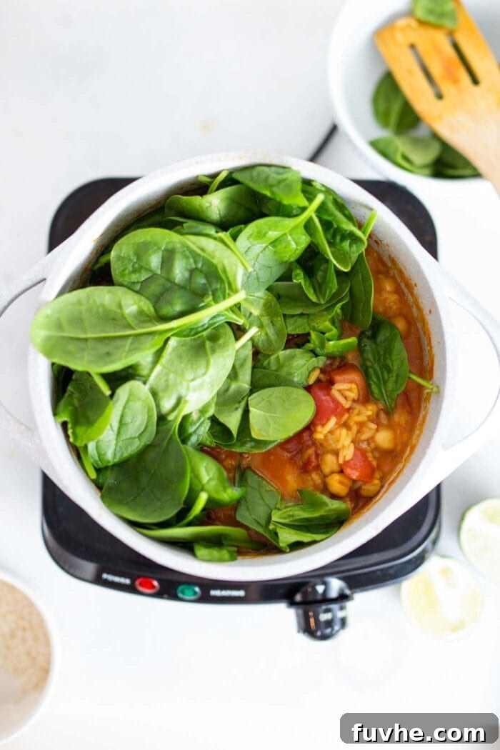 Iron Rich Vegan Foods 11 Spinach being stirred into a thick tomato stew in a pot.