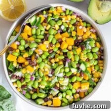 A large bowl of mango, corn, edamame and cucumber salad with a sliced avocado beside it.