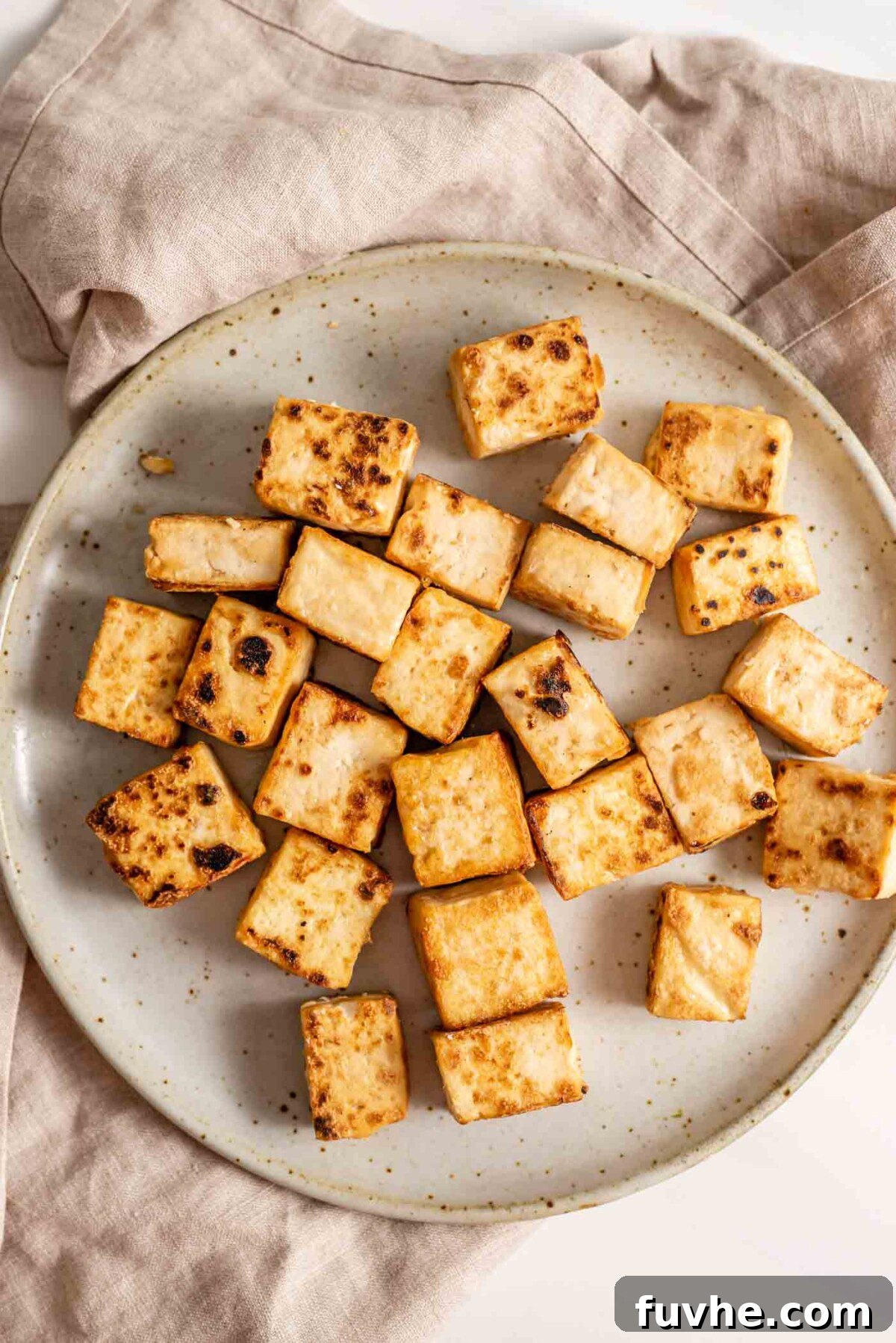 Crispy, golden-brown tofu cubes resting on a plate after frying.