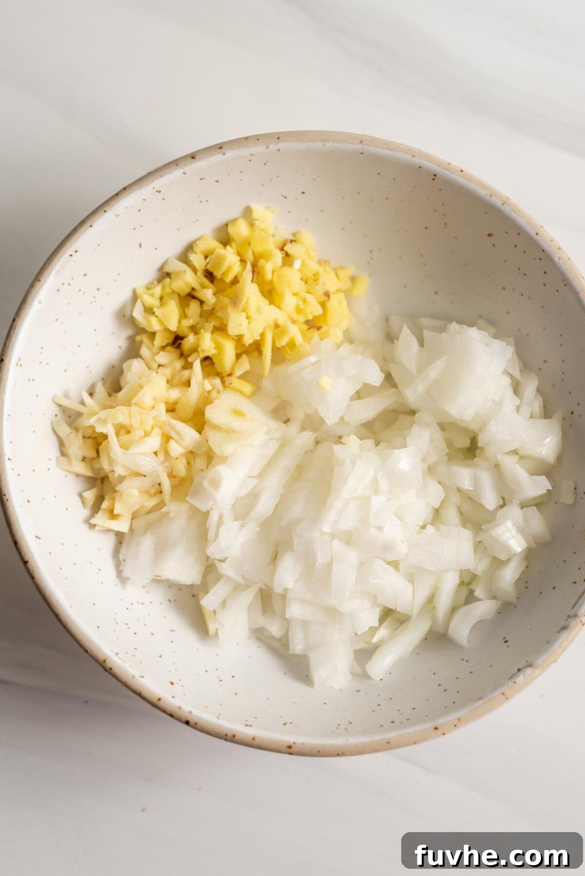 A small bowl filled with freshly chopped onions, minced ginger, and minced garlic.