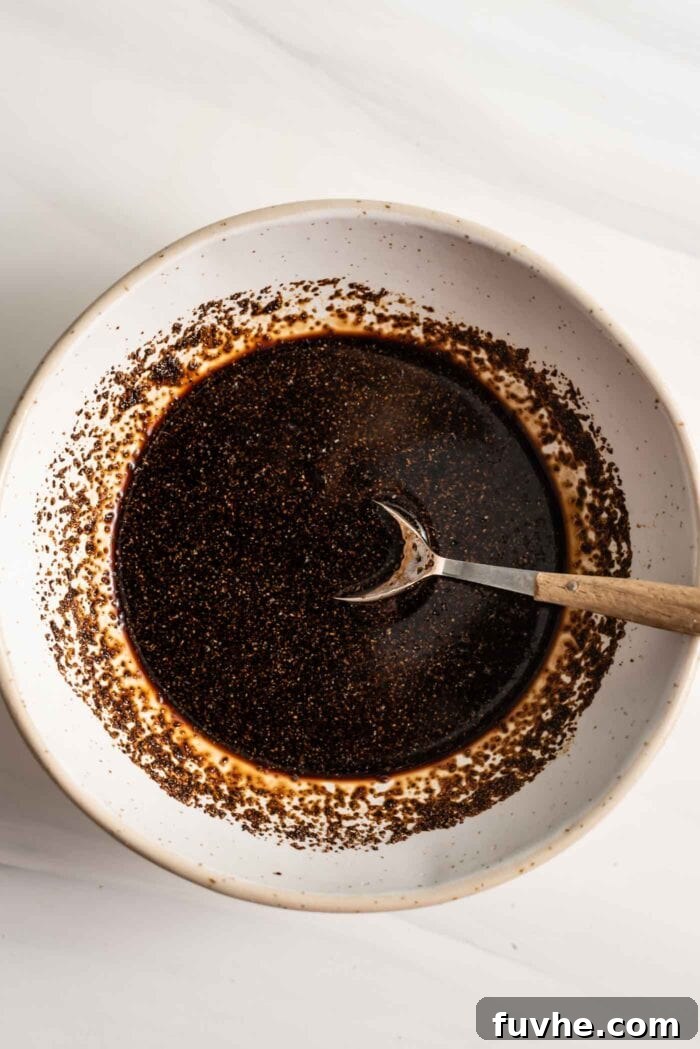 A bowl of glossy black pepper sauce with a spoon, ready to be added to the pan.