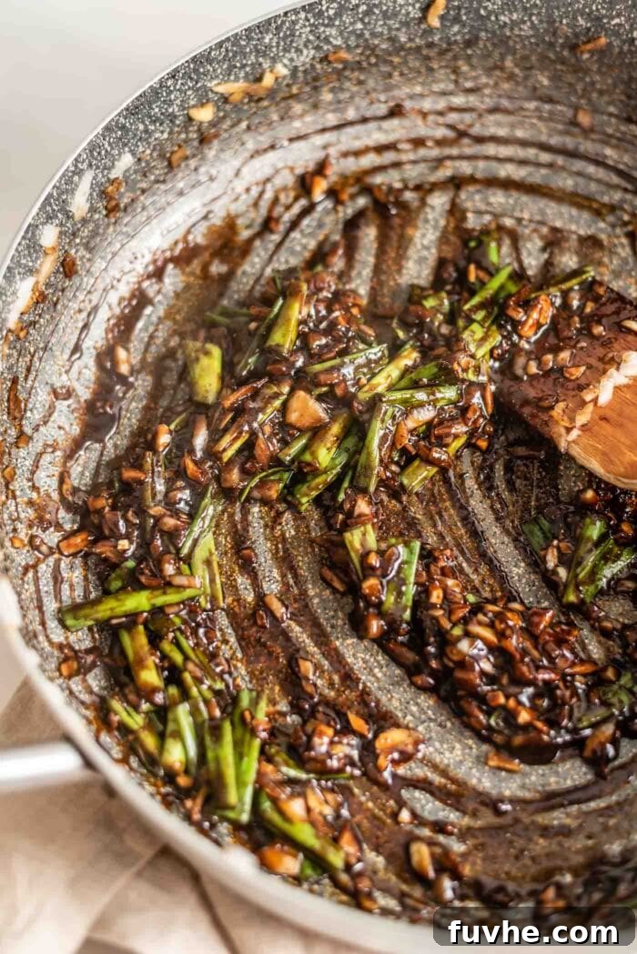 Scallions, onions, ginger, and garlic simmering in a dark, thick sauce in a hot pan.