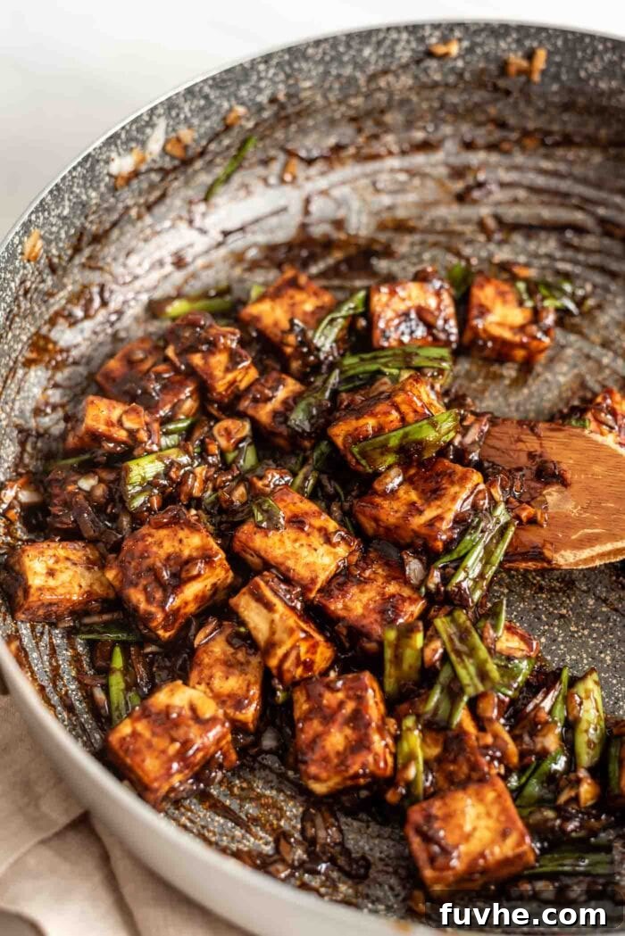 Tofu cubes mixing with black pepper sauce, onions, garlic, and ginger in a pan.