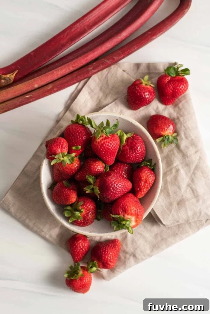 A vibrant display of fresh strawberries beside several stalks of crisp, red rhubarb, ready for baking.