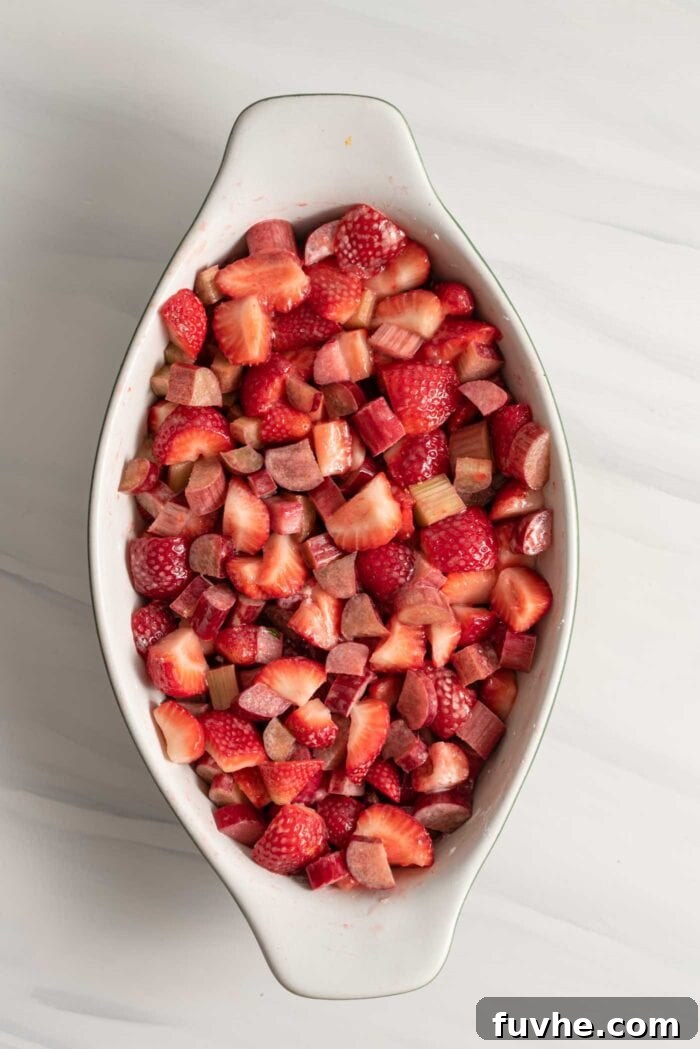 Freshly chopped strawberries and rhubarb mixed with sugar and cornstarch in a glass baking dish, ready for the topping.