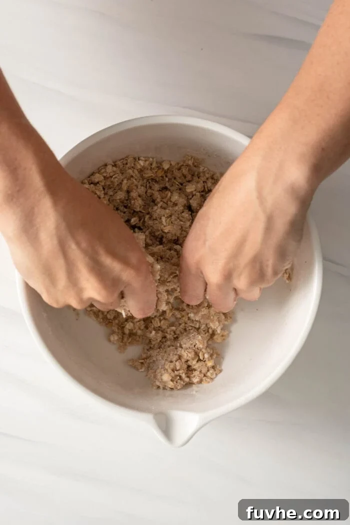 Close-up of two hands expertly mixing a crumbly oat topping mixture in a bowl.