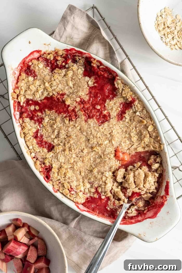 A freshly baked strawberry rhubarb crisp in an oval baking dish, with a serving spoon resting in it.