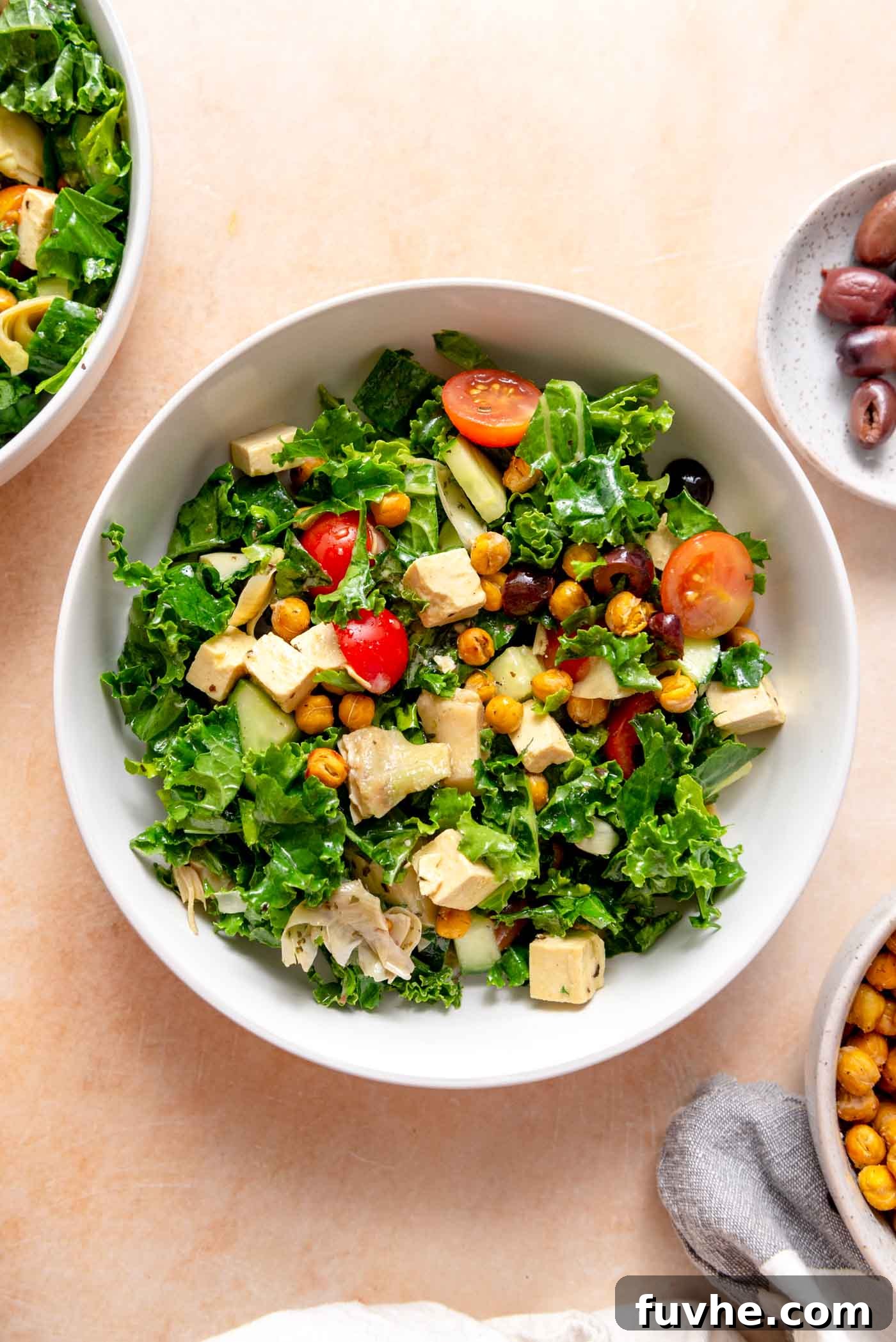 A vibrant Mediterranean kale salad in a bowl, featuring chopped tomatoes, marinated artichoke hearts, crisp cucumber, briny Kalamata olives, and creamy tofu feta cubes.