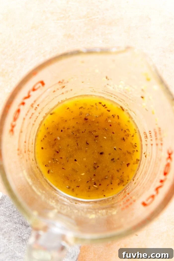 A small glass measuring cup filled with a golden, zesty vinaigrette salad dressing, ready to be poured over fresh greens and vegetables.