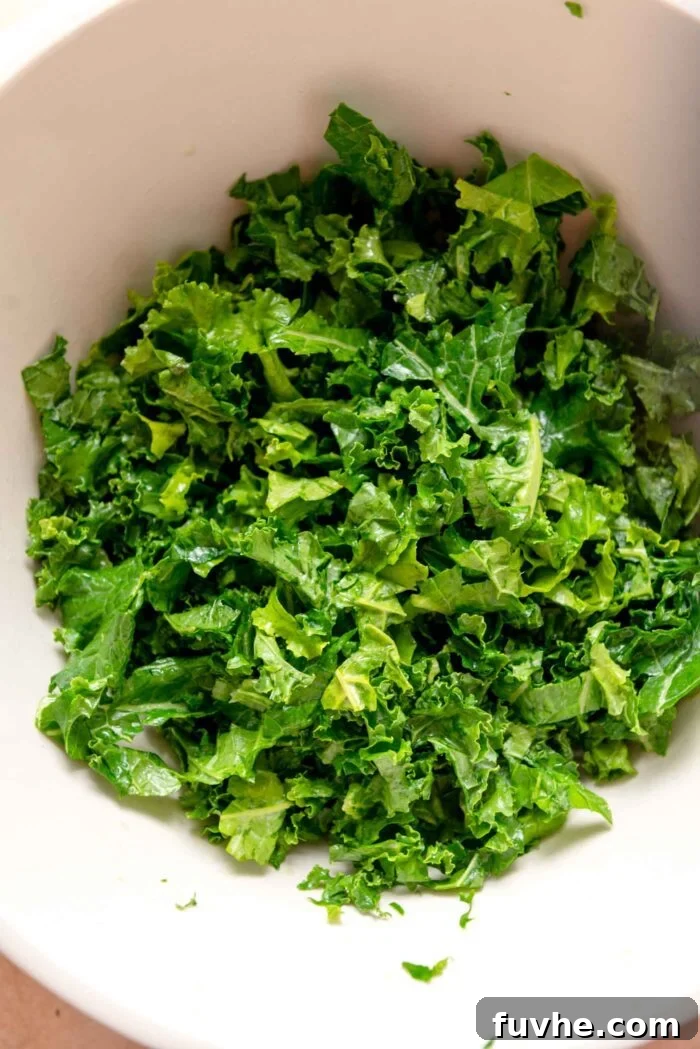Freshly chopped kale, glossy and dark green, after being massaged with olive oil, lemon juice, and salt in a large mixing bowl, ready for other ingredients.