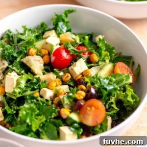A beautifully arranged bowl of Mediterranean kale salad, featuring crumbles of feta, vibrant tomatoes, crisp cucumber, briny olives, roasted chickpeas, and tender artichoke hearts, ready to be enjoyed.