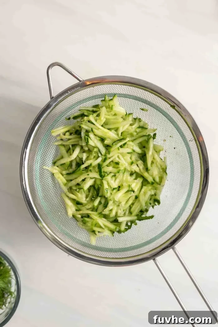 Finely grated cucumber sprinkled with salt, resting in a colander set over a sink, allowing excess water to drain away.