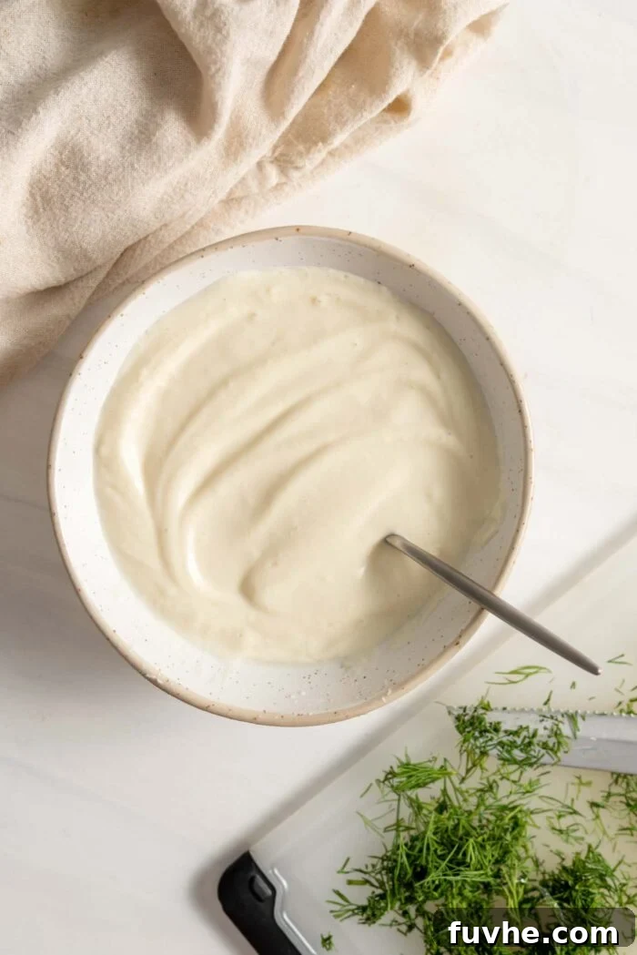 A creamy, white, blended tofu mixture in a bowl, with a spoon resting inside, showcasing its smooth texture before adding other ingredients.