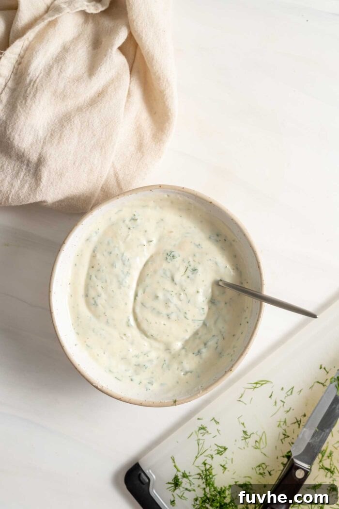 A creamy, white tzatziki base infused with finely chopped fresh green dill, in a bowl with a spoon, highlighting the vibrant herb.