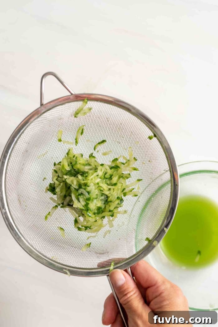 A close-up of thoroughly drained, grated cucumber in a colander, showing minimal moisture, indicating it's ready for mixing.