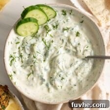 A bowl of creamy vegan tzatziki dip with a spoon in it, garnished with fresh dill.