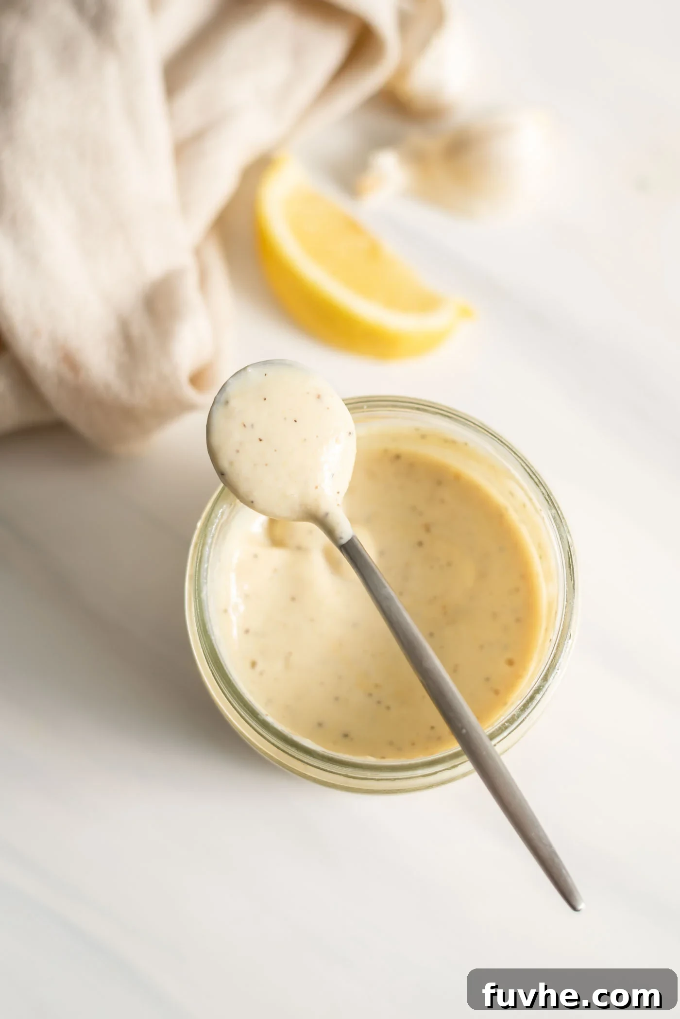 A spoonful of creamy vegan caesar dressing resting on a jar of dressing.