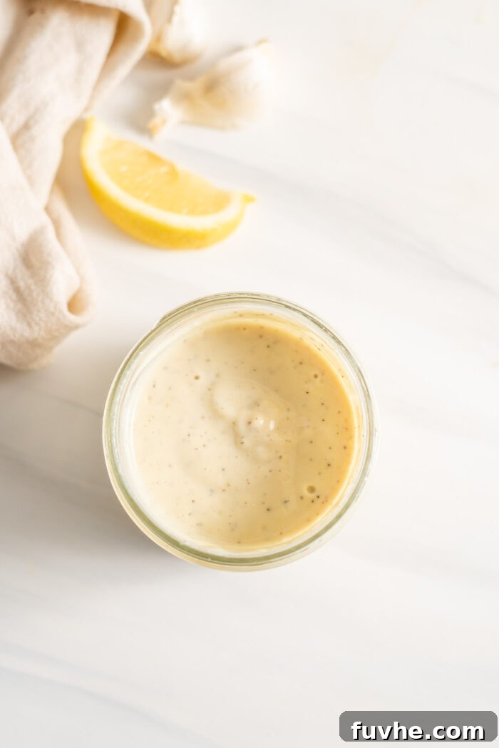Creamy vegan caesar salad dressing in a jar with a lemon slice beside it.