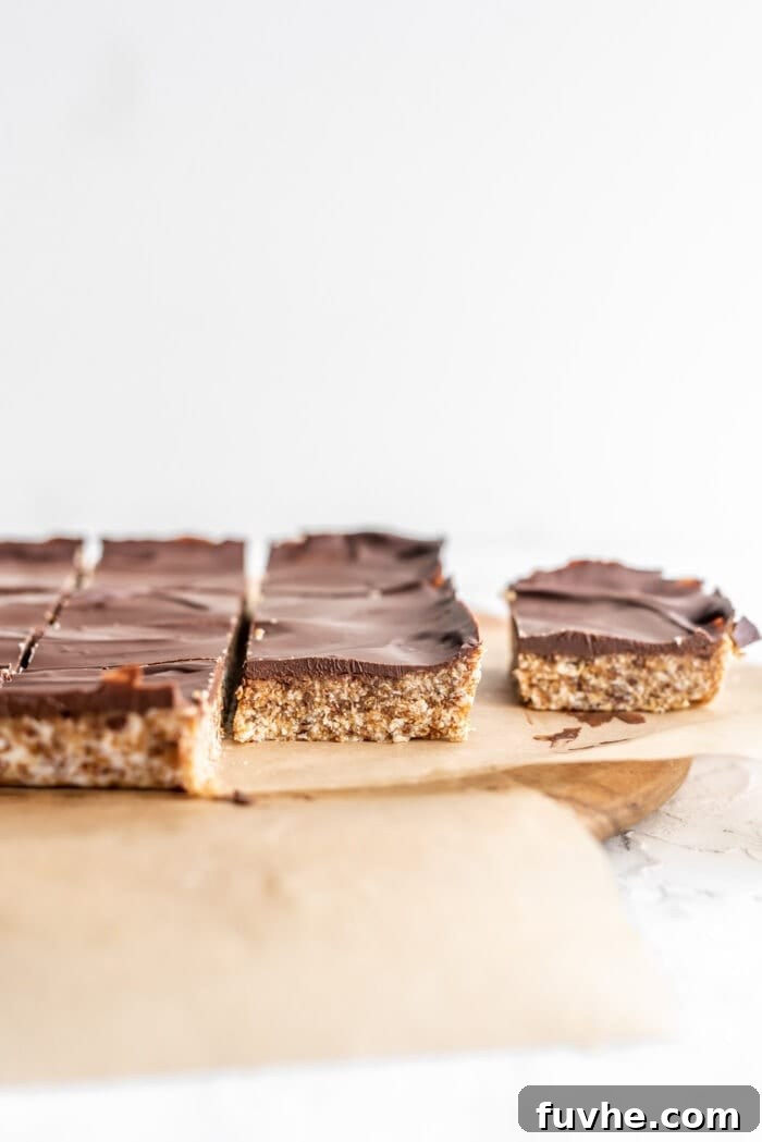 Decadent Plant-Based Chocolate Coconut Squares 11 Front view of chocolate topped coconut date bars on parchment paper, showcasing the textured base and smooth chocolate layer.