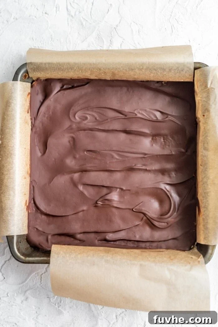Decadent Plant-Based Chocolate Coconut Squares 8 Chocolate-covered coconut bars chilling in a baking pan lined with parchment paper, fully set and ready for slicing.
