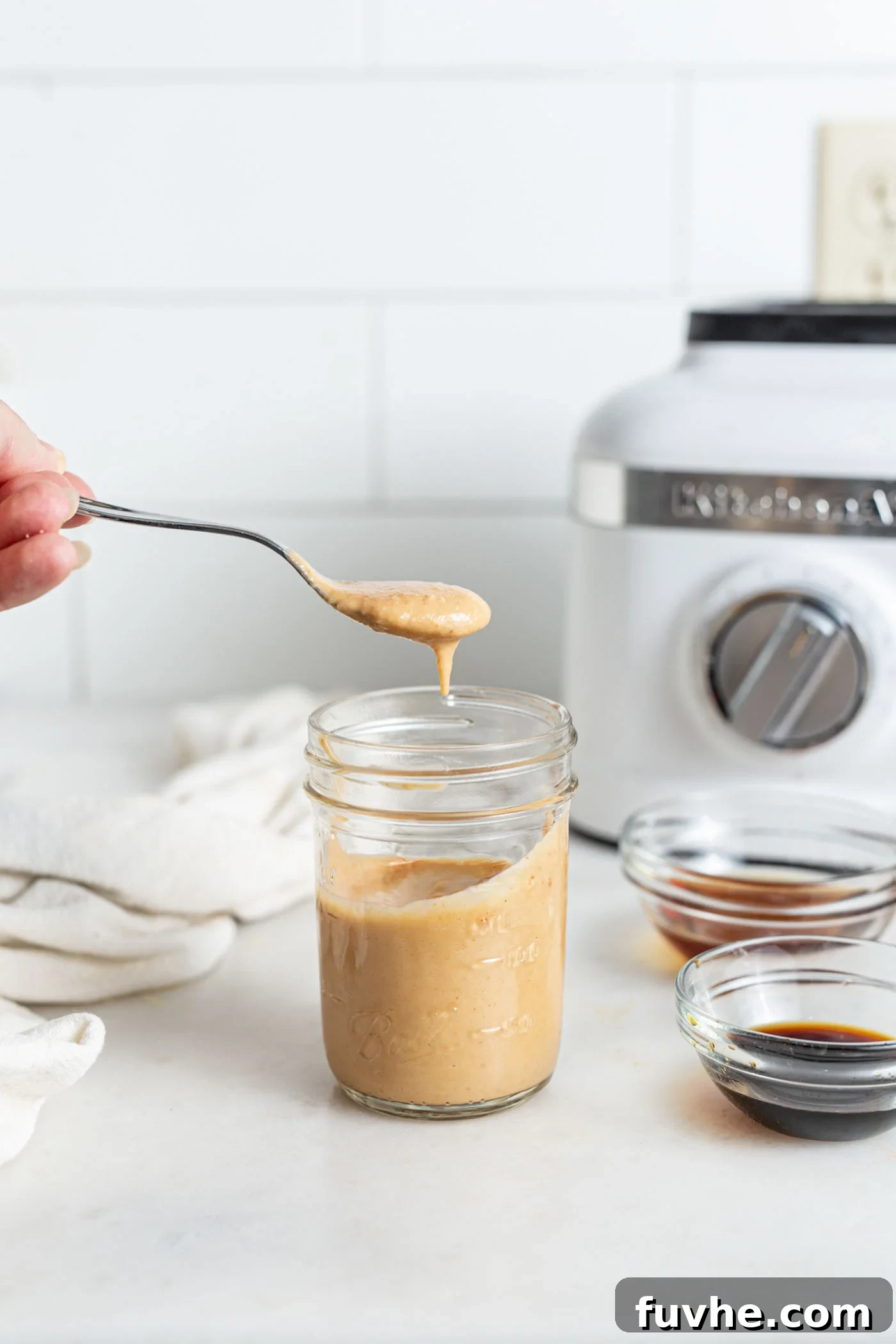 A spoonful of rich, creamy vegan spicy mayo being scooped from a small jar, showcasing its smooth texture and vibrant color.